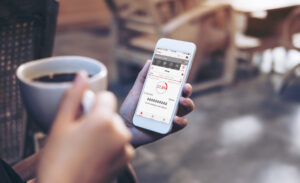 woman's hands holding white mobile phone with energy management system on screen drinking coffee in modern loft cafe