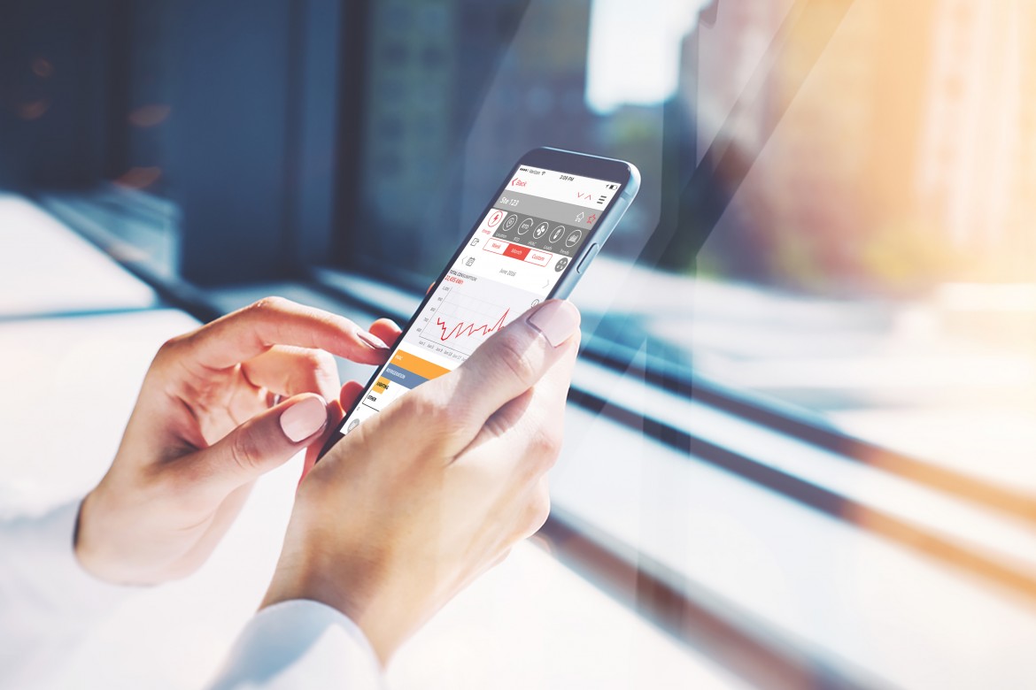 Hands holding a cell phone close to a window using an energy management mobile app